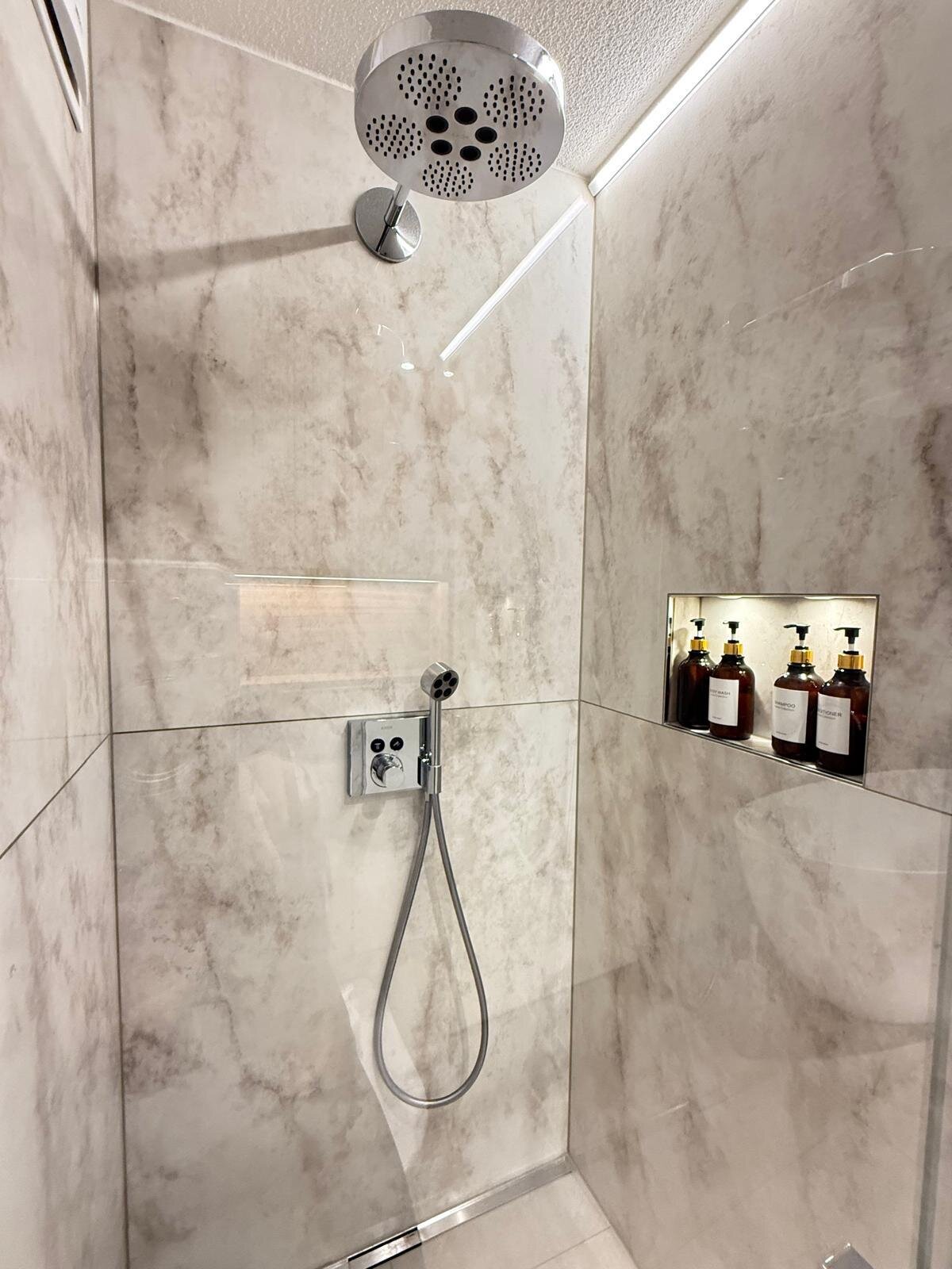 Bodenebene Dusche mit Regenbrause und Nische für Pflegeprodukte, Wände in Marmor-Optik