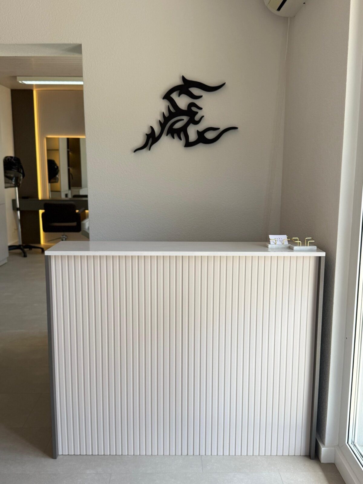 Empfangstheke mit gerillter Front und dem Salon-Logo an der Wand