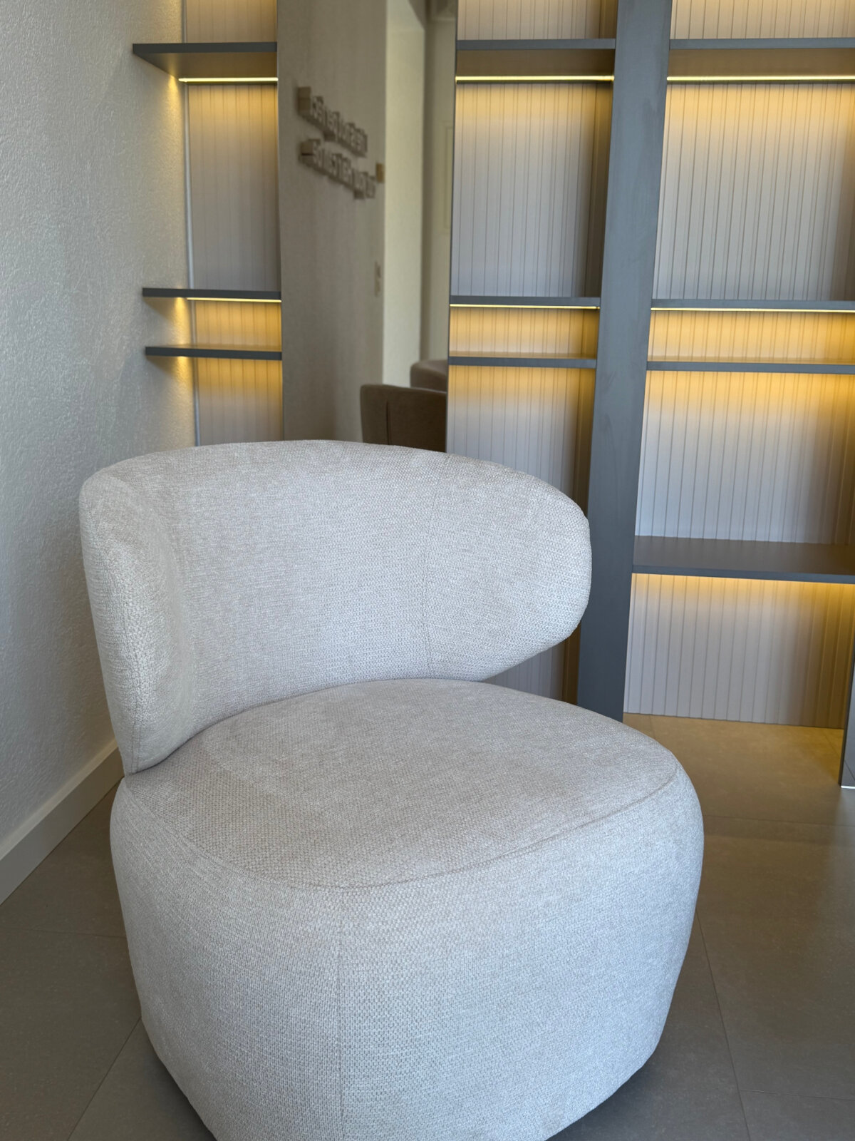 Bouclé-Sessel vor der beleuchteten Regalwand aus geriffeltem Glas